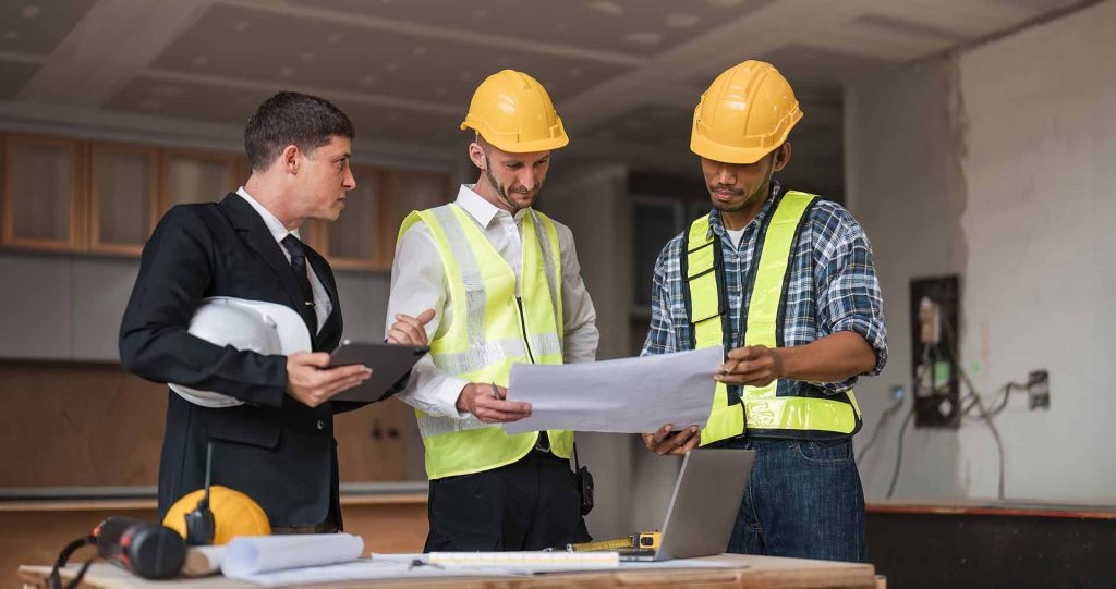 3 men at construction site, looking at blueprints